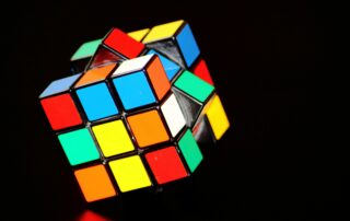 dua kubus Rubik, satu yang telah diselesaikan dan satu yang belum. Kubus yang telah diselesaikan memiliki warna yang seragam di setiap sisi, sedangkan kubus yang belum diselesaikan memiliki warna yang acak. Kedua kubus tersebut terletak di atas permukaan yang gelap,