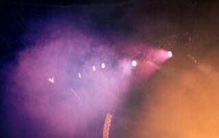 bagian atas panggung konser dengan pencahayaan yang dramatis. terdapat lampu sorot dengan berbagai ukuran dan warna sehingga menghasilkan cahaya yang berwrna warni