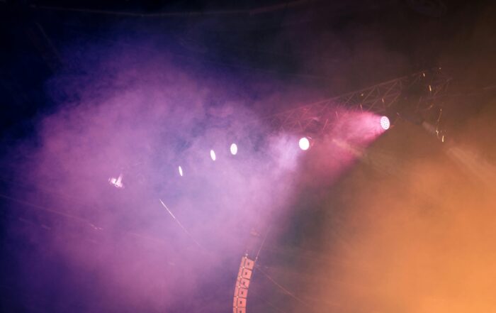 bagian atas panggung konser dengan pencahayaan yang dramatis. terdapat lampu sorot dengan berbagai ukuran dan warna sehingga menghasilkan cahaya yang berwrna warni