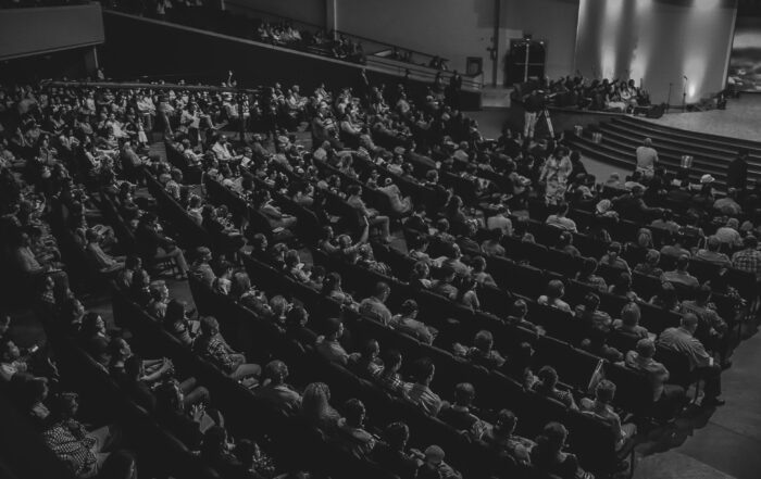 Ruangan auditorium dengan kursi beringkat seperti amphiteater dengan panggung bercahaya di depannya-teks MC formal