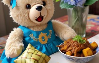 seekor boneka beruang berwarna krem yang mengenakan gaun berwarna biru cerah dengan hiasan emas. Boneka beruang tersebut memiliki pita berwarna biru muda di telinganya. Di depannya, terdapat semangkuk hidangan berwarna cokelat kekuningan dengan potongan tahu dan taburan peterseli, serta beberapa kerupuk berwarna krem. Di sebelah kiri boneka beruang, terdapat ketupat yang terbuat dari anyaman janur berwarna hijau dan kuning. Latar belakang gambar menampilkan vas bunga berisi bunga hydrangea berwarna biru dan bunga mawar berwarna merah muda dan putih. Meja tempat semua objek diletakkan memiliki taplak meja dengan motif geometris berwarna merah, biru, dan putih.